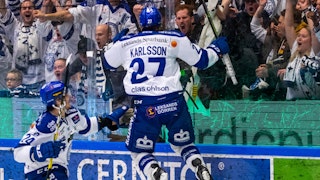 Leksands Anton Karlsson i vit tröja och blåa byxor hoppar i glädje upp mot plexiglaset framför extatiska hemmafans